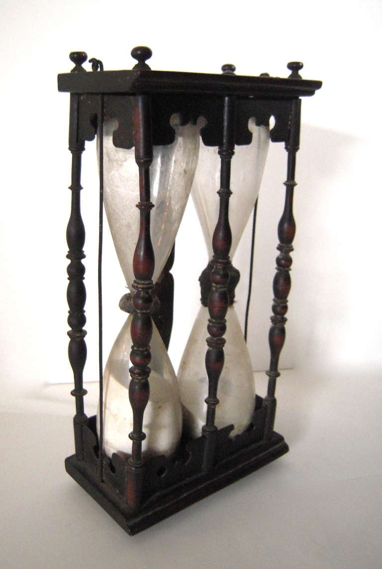 An 18th century English double hourglass, with two double-bulbed glass ampules containing white sand, the centers joined by twine and wax, mounted in a dark stained oak stand with five baluster-turned spindles, with shaped crest and bottom