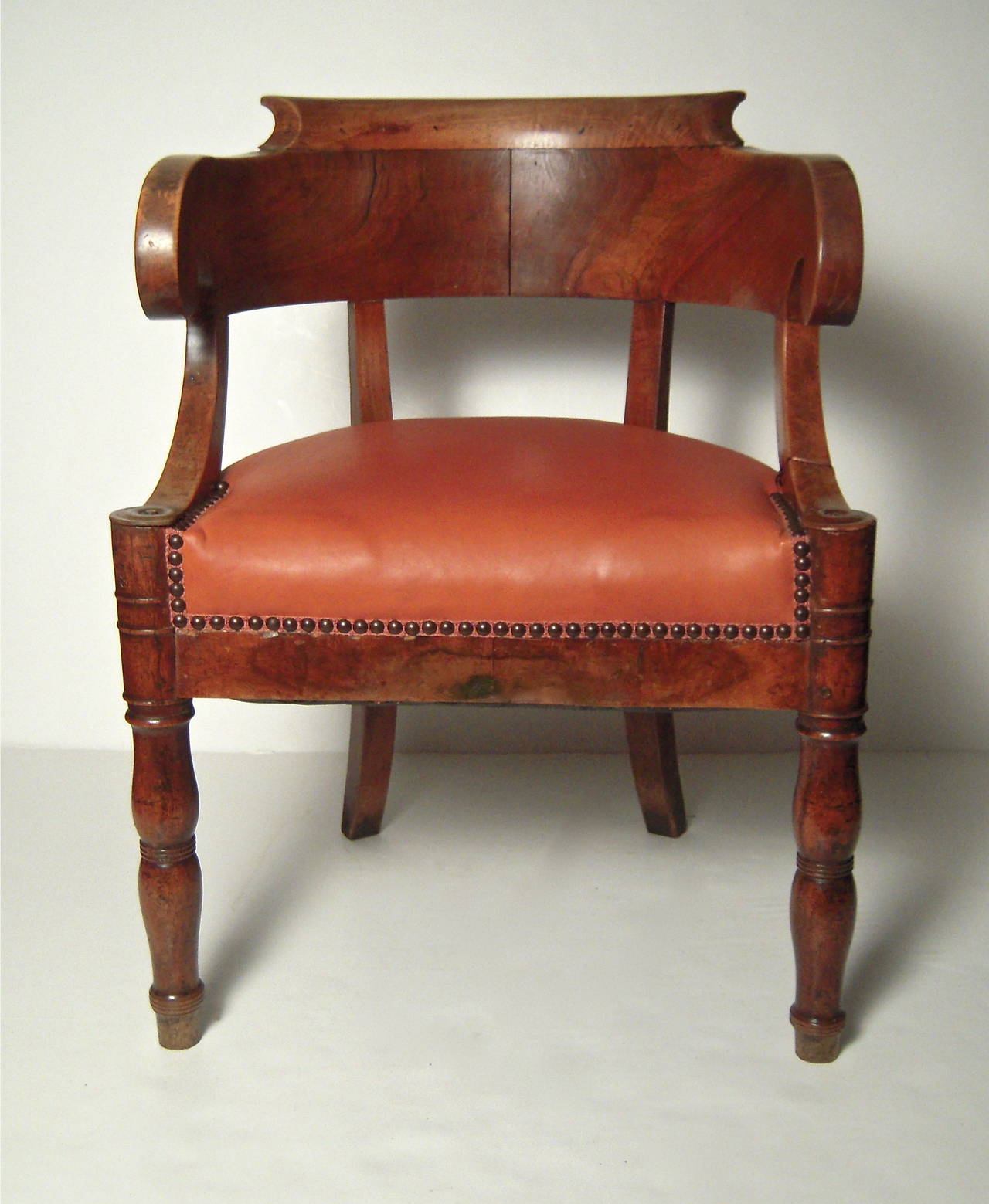 A French Empire period arm chair, of wonderful sculptural form in richly figured and carved walnut, the curved back with scrolled arms over downswept supports, the semi circular leather upholstered seat over baluster turned legs.
Perfect as an
