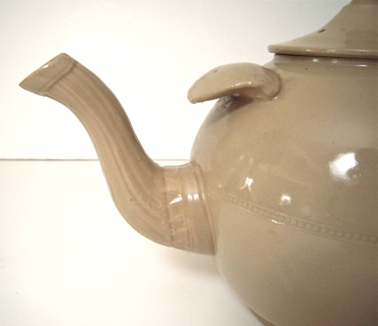 A giant, oversized stoneware teapot, or punch pot, English, circa 1880s, in glazed buff colored earthenware with impressed decorative band around the center and on the fluted spout, with substantial finger support for pouring, above the
