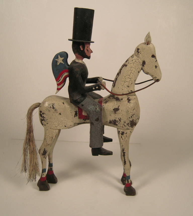 A folk art sculpture of winged Abraham Lincoln in a stovepipe hat on horseback in carved and painted wood with horsehair tail  by artist William H. Roy. signed.

Provenance: A private Massachusetts collection. Purchased at the Museum of American