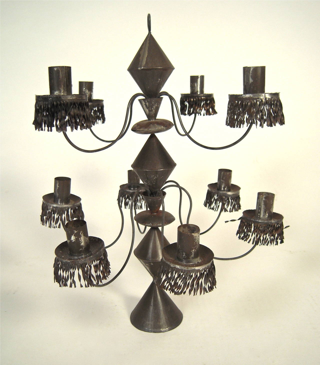 A pair of Mexican ten-light tin candelabra, each with conical bases, the bobeches for each candle decorated with finely cut and twisted tin fringe.
Each candelabrum also has a ring holder on top for hanging. This pair was purchased in Mexico in the