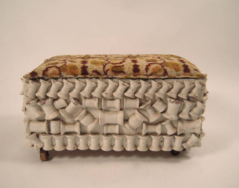 An unusual and artfully made Folk Art footstool, of rectangular form, the four sides composed of an artful composition of sections of spools of thread, painted white, the top made with a section of wool carpet in shades of cream, green, ocher and
