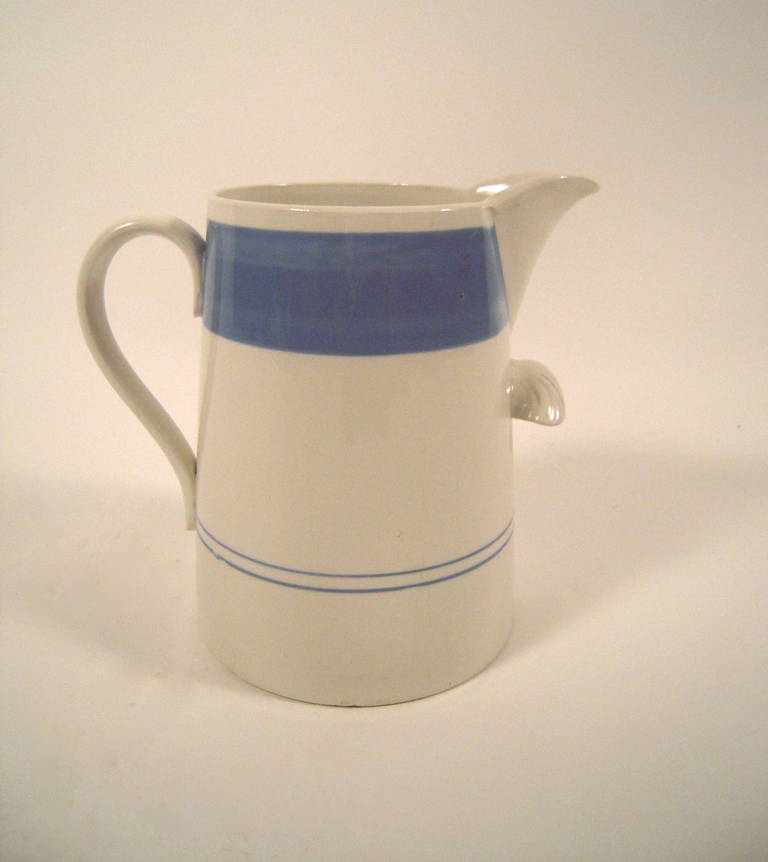 A giant Staffordshire pitcher, glazed in white and decorated with a wide blue band at the top and parallel blue bands at the bottom, with finger support underneath the spout for ease in handling.