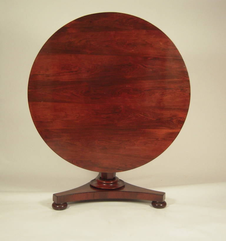 An English Regency period rosewood circular center, or dining table, circa 1820-30, raised on a tapered and paneled standard,  terminating in a circular ring on a triangular plinth base, raised on three bun feet.

Height 28