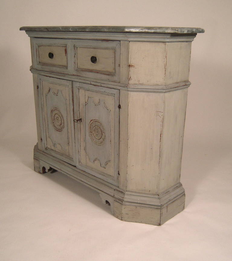 A well proportioned Italian blue and grey painted Renaissance Revival side cabinet, Italian, circa 1880, the faux marble painted top with canted corners over 2 drawers above a pair of cupboard doors each centered by a carved rosette within a shaped