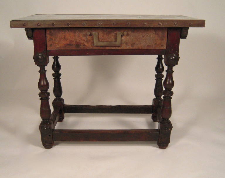 A character filled Spanish Baroque style table, with period 17th century walnut base, the baluster turned legs joined by cross stretchers, the rectangular, distressed mirrored top, banded with patinated iron with raised studs, centered by a frieze