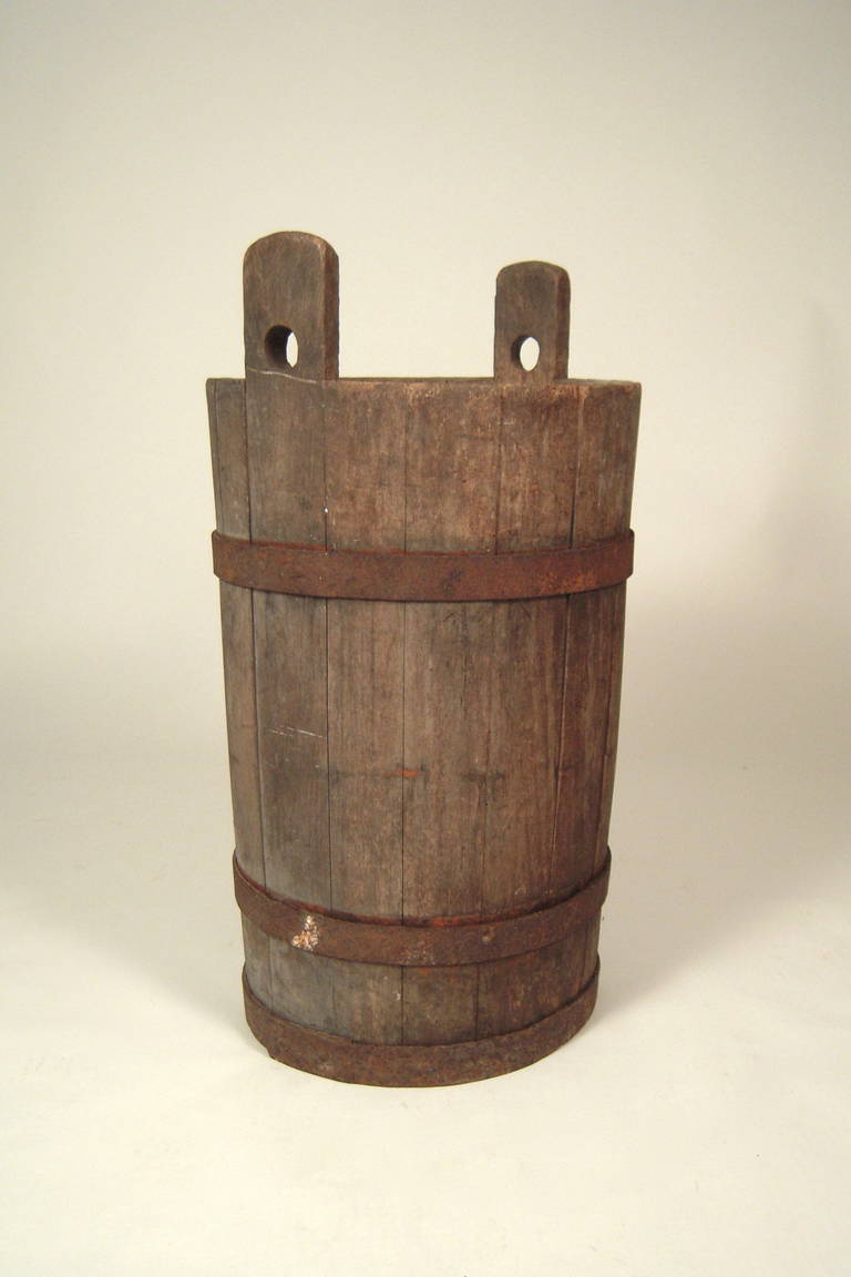 A tall, decorative European (German) country farm bucket, the slats of wood bound with iron bands, with 2 projecting slates with holes cut out for a carrying handle.  With a liner or pail inside, this bucket makes for a beautiful container for