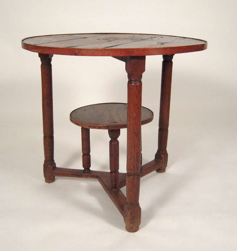 An English Country 2-tiered  round occasional table in oak, the banded circular, top supported by 3 cylindrical turned legs joined by 3 stretchers centered by a circular shelf raised on 3 conforming legs.

Provenance: Stillington Hall, Gloucester,