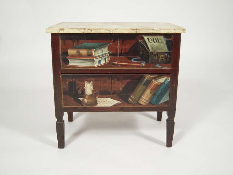 A small, beautifully faux painted wood Italian chest, perfect in scale, for a side table next to a chair, the faux marble painted top over two drawers painted with a trompe l'oeil depiction  of books and other objects on the front and sides, raised