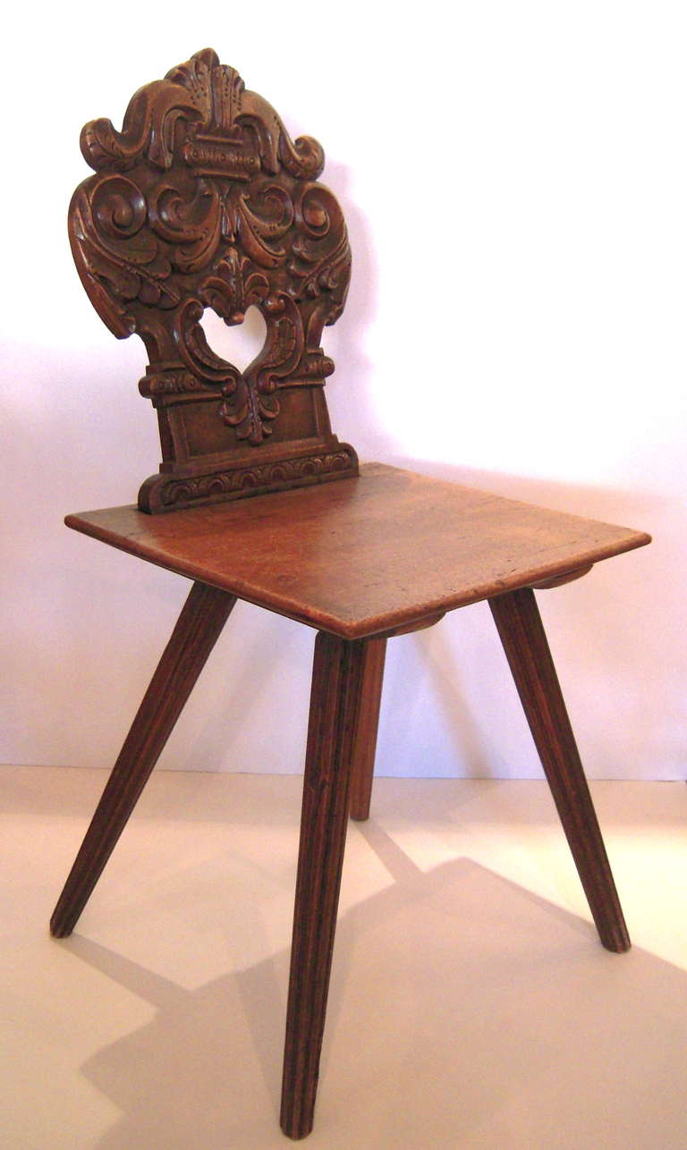 A 19th century hand carved Swiss Alpine side chair in walnut, theshaped back with well carved foliate and scrolled decoration with decorative heart cut-out above a nearly square shaped seat raised on 4 splayed, carved fluted tapering legs.