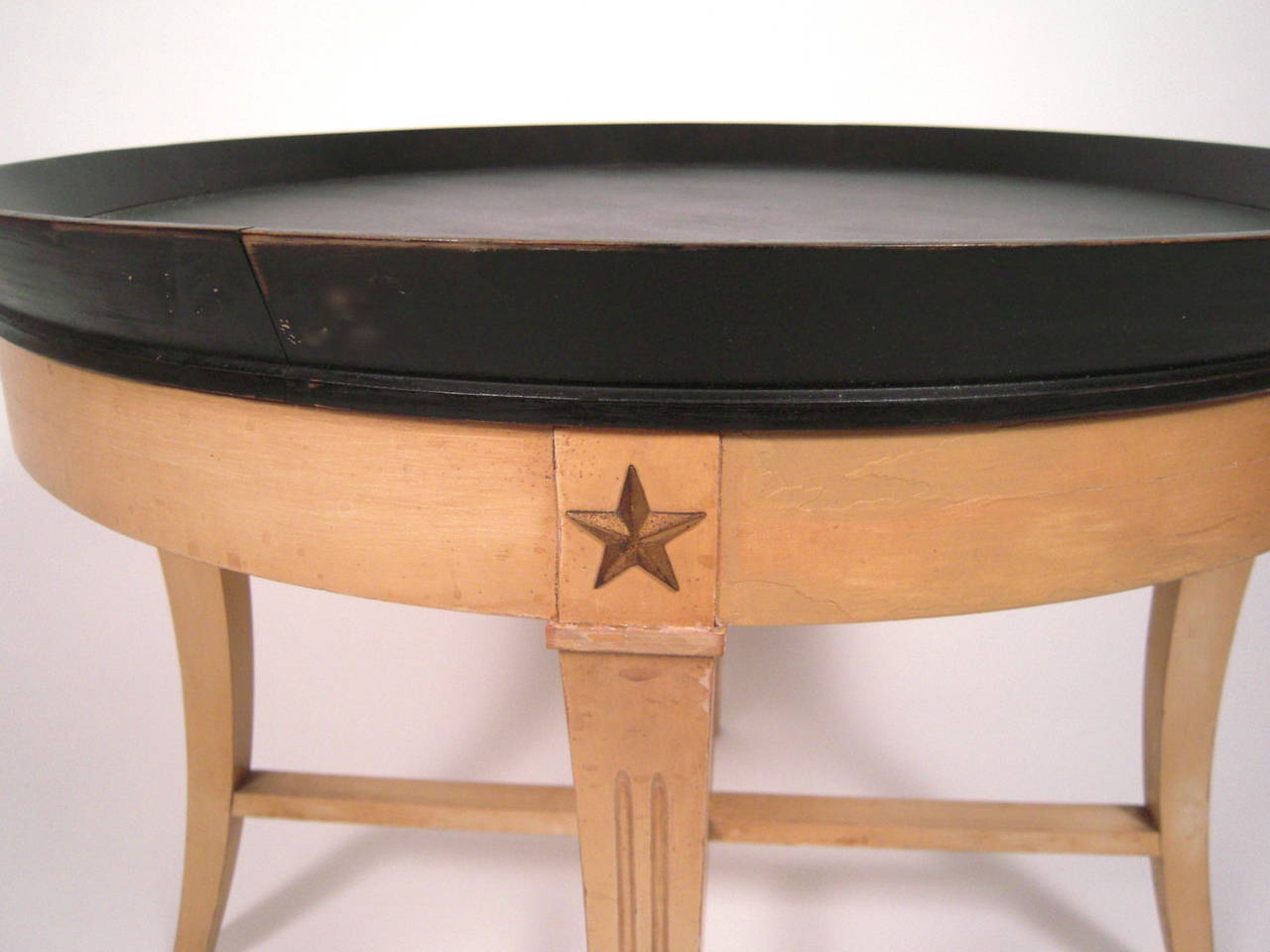 A Kittinger round tray top coffee table, with removable black painted top on a conforming cream colored base, the fluted splayed legs headed by applied brass stars and joined by cross stretchers. Retaining original maker's label on underside.