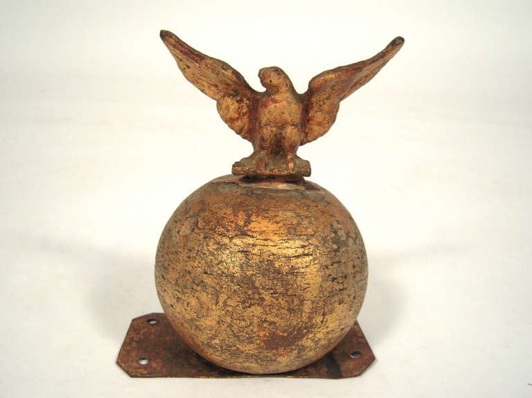 A gilded cast metal eagle with wings spread wide, perched on a globe, likely a finial or flag topper.