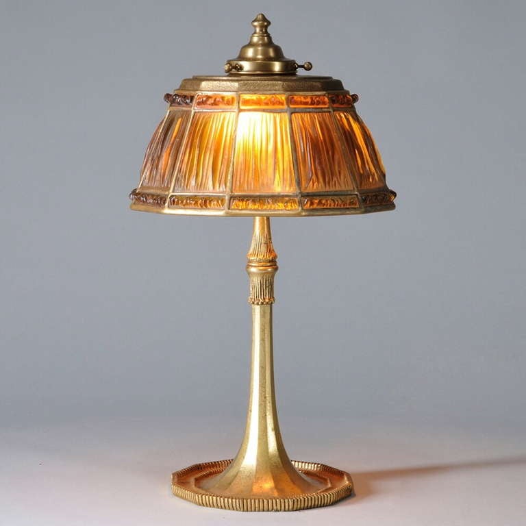 A fine Tiffany table lamp, with gilt bronze (bronze doré)  paneled columnar support with a spreading, reeded 12-sided base, the shade with amber colored 