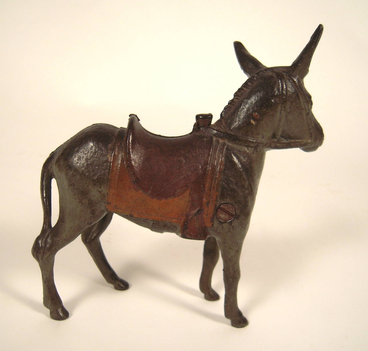 A beautifully patinated and well modeled cast iron coin bank in the form of a donkey, in all original paint, with muted red and yellow saddle, circa 1920s-1930s.