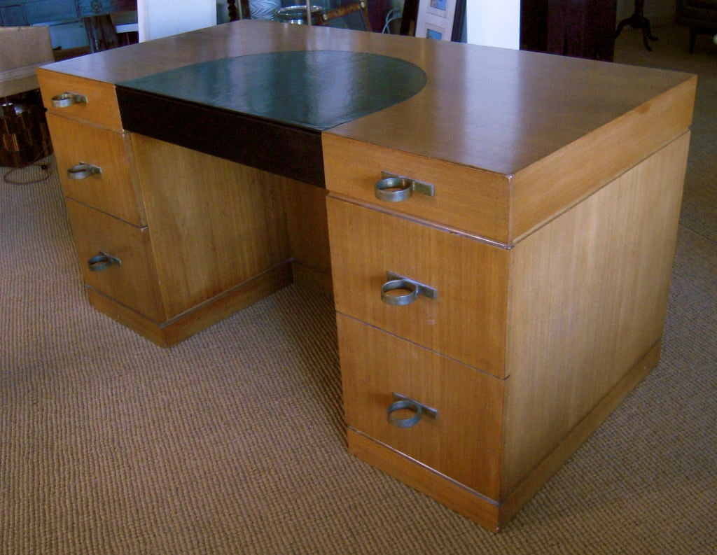 A striking Art Deco period desk in light mahogany with inset black leather semi circular top and frieze drawer front , each pedestal with 3 graduated drawers with over graphic and unusual large brass ring drawer pulls, the back side of the desk with