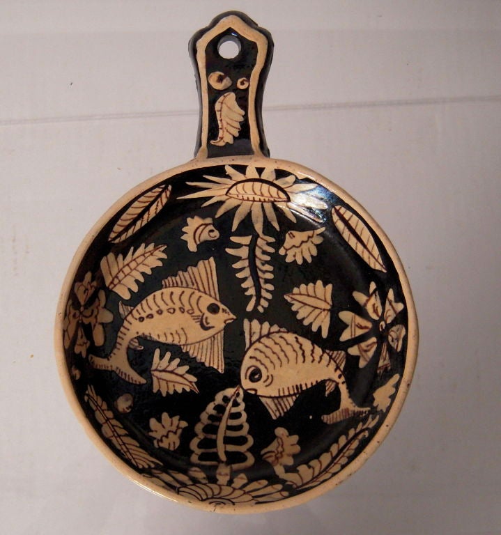 A vintage Mexican hand potted and glazed ceramic Migas pan, decorated with fish and floral design in cream on a black ground.