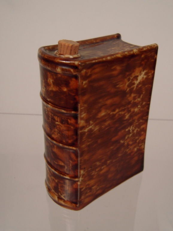A Rockingham pottery book-form ceramic flask in mottled brown 'tortoise shell' glaze, with impressed 'Departed Spirits' book title on the spine and cork stopper.