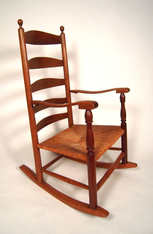 A 19th century American ladder back rocking chair in well patinated oak (or ash?), with rush seat. Charming, quirky, but well crafted, design details as seen in arms. Wonderful, soft wear to cross stretcher as seen in View 8 and blades in View 7.