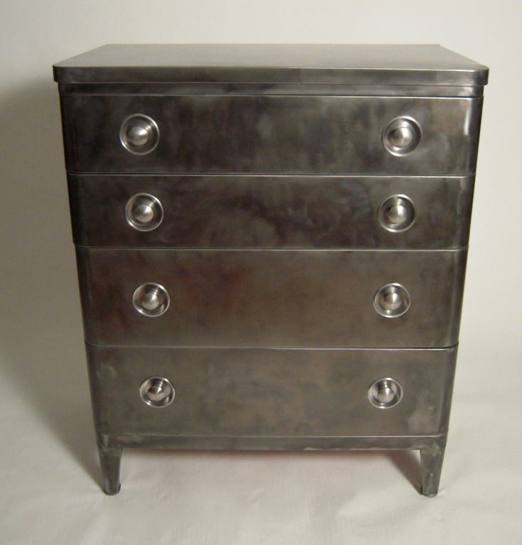 A stylish gunmetal grey stainless steel dresser designed by Norman Bel Geddes with rounded corners, 5 graduated drawers and circular drawer pulls in contrasting polished metal.
