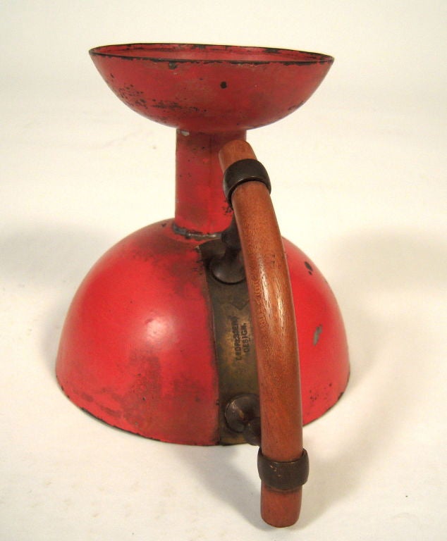 A Christopher Dresser (1834-1904) Kordofan chamber candlestick in red painted tin, the dished drip tray above cylindrical neck on a domed base with curved cylindrical mahogany handle. Signed with the  factory mark of Richard Perry, Son & Co.,