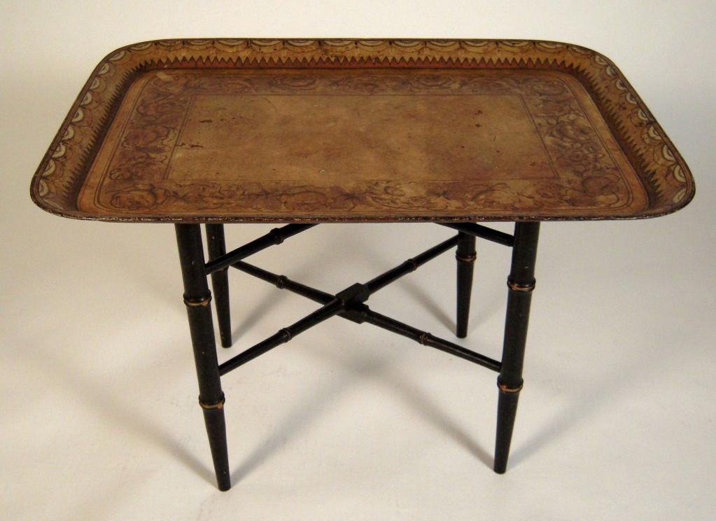 An early 19th English rectangular tole tray on stand, the tray painted overall in gold on black with inner floral and foliate  band and outer geometric and swag band, on a later ebonized faux bamboo X-form stand.