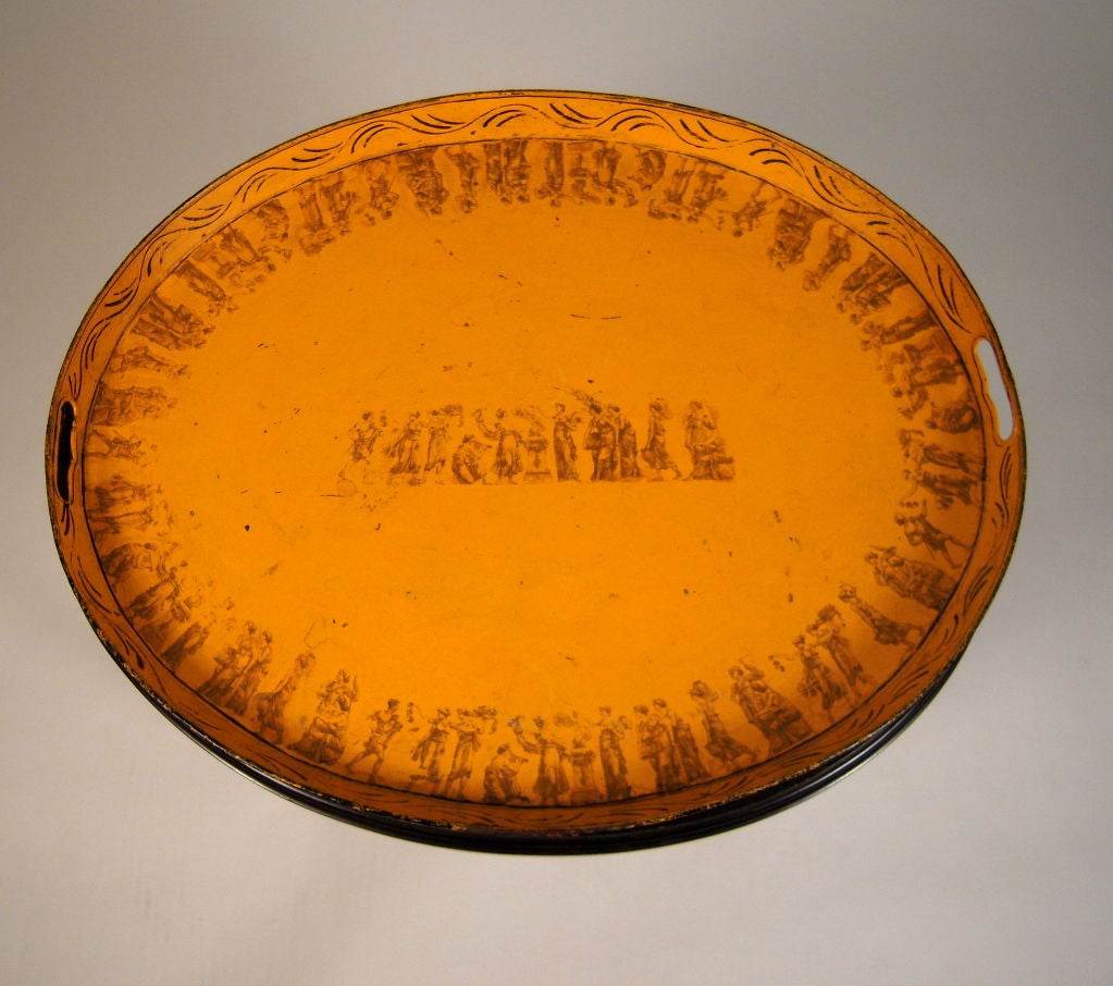 An early 19th century French yellow oval tole tea tray decorated with hand painted and transfer printed neoclassical ornament, on a later ebonized stand with turned faux bamboo legs joined by an X-shaped stretcher.