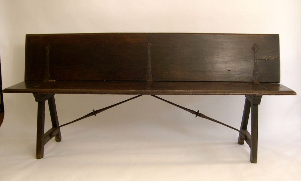 An 18th century Spanish baroque folding bench in solid walnut and wrought iron, the 2 solid plans of walnut joined by their original wrought iron strap hinges on A-shaped trestle supports joined by wrought iron radial stretchers. This bench must