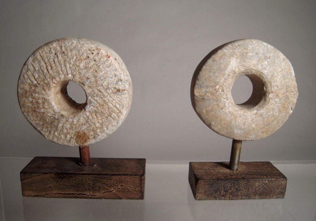 Two carved mill stones, mounted on patinated metal rectangular plinths.<br />
Millstones were used in windmills and watermills, including tide mills, for grinding wheat or other grains.