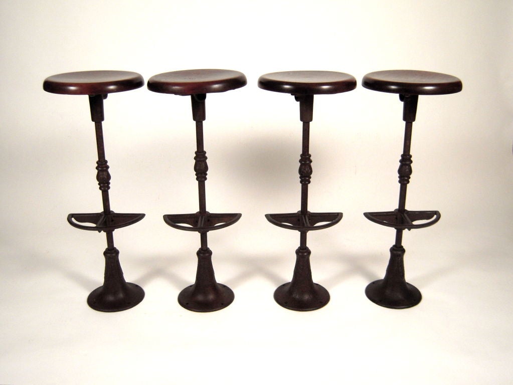 A set of 4 vintage ice cream parlor stools with swiveling circular walnut seats on acanthus leaf-decorated cast iron bases with foot rests.