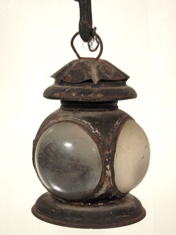 An unusual black painted metal railroad lantern with 3 convex frosted glass lenses, hanging from an associated heavy gage wrought iron chain. Ideal for a hallway, powder room or other small space, or as a decorative table top lamp.