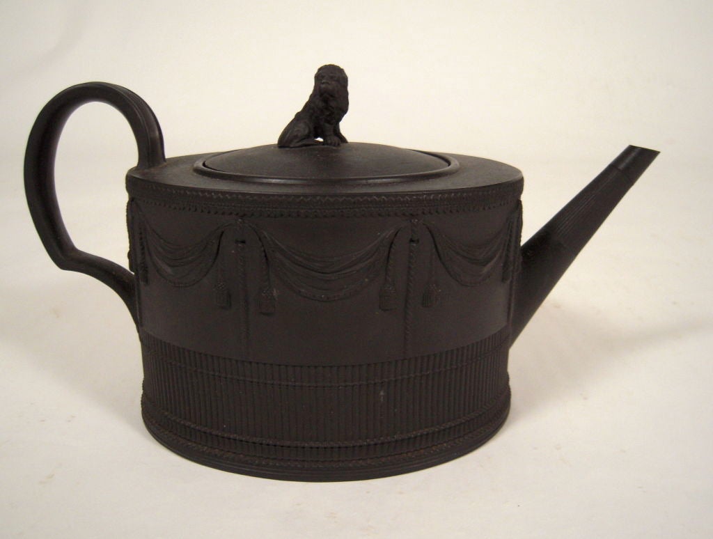 A Neale and Company English stoneware black basalt teapot, circa 1790-1800, the cover with seated lion knop, the pot of oval form decorated with molded linen fold swags and tassels over a fluted band, the strap handle decorated with acanthus leaves.
