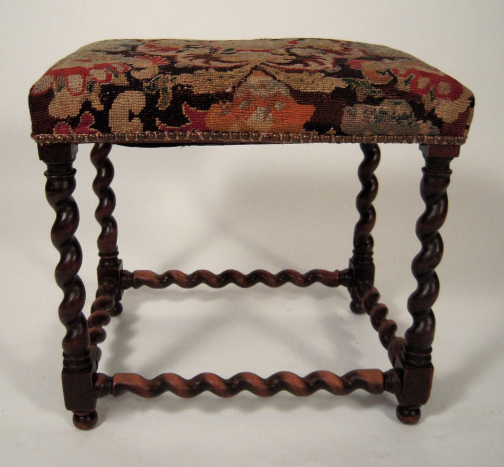 A Jacobean style stool in walnut, the richly colored early,  floral gros point tapestry upholstered top raised on 4 barley twist legs joined by conforming stretchers, all raised on 4 small ball feet.