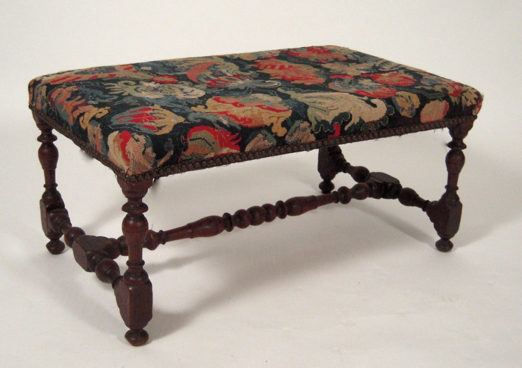 A Jacobean style foot stool or low bench in turned, dark stained oak with needlepoint tapestry upholstery