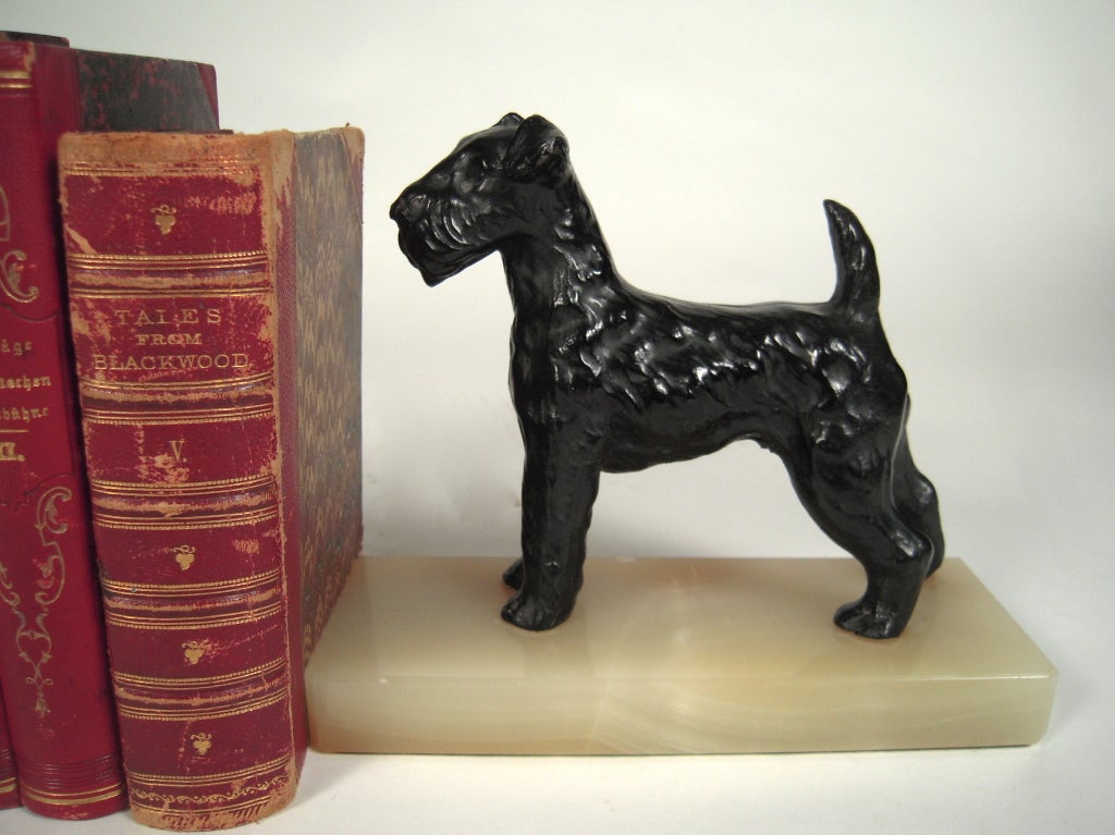 A pair of black painted, cast iron terrier figural bookends, mounted on rectangular onyx plinths.