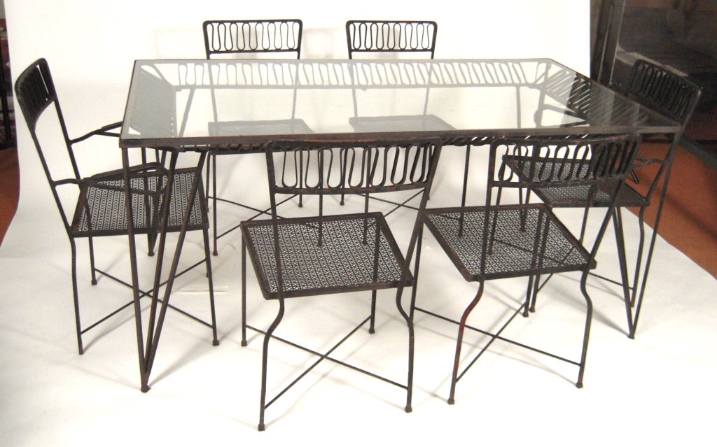 A stylish 1940s wrought iron garden 'Ribbon' dining table and chairs designed by Maurizio Tempestini for Salterini (active, NY 1928-1953), comprising a glass top rectangular dining table, 4 side chairs and 2 arm chairs.

Table: H: 29 5/8