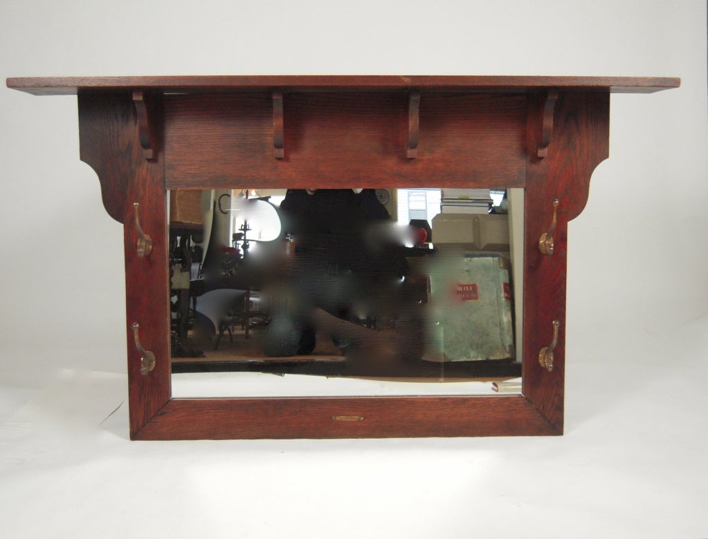 An Arts & Crafts period architectural mirror, with shelf supported by brackets and well modeled copper finished hat and coat hooks, retaining a small brass plaque 