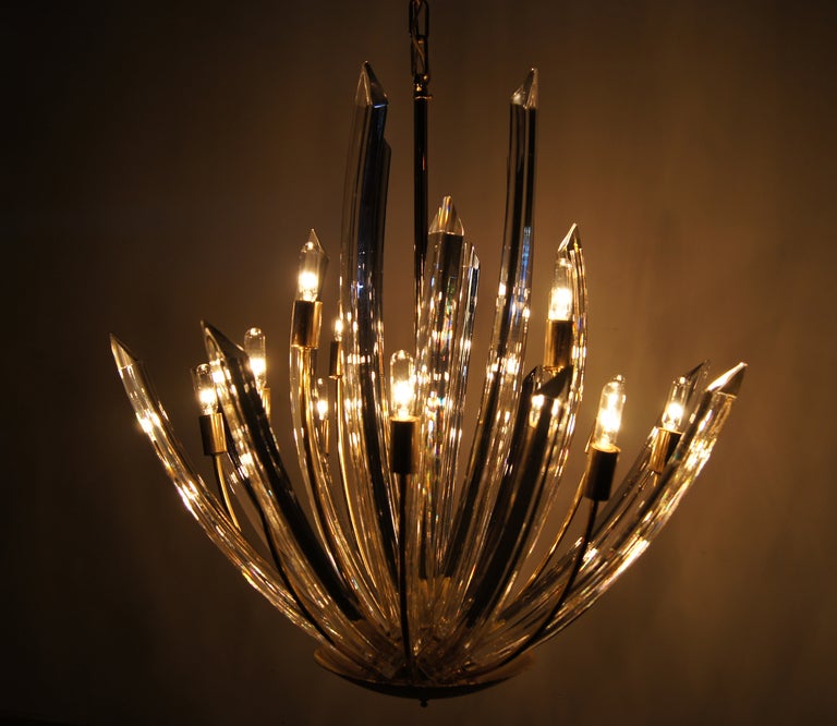 This large and impressive Murano chandelier features twelve light fixtures dispersed amongst 16 curved glass rods that beautifully capture and redistribute the light.