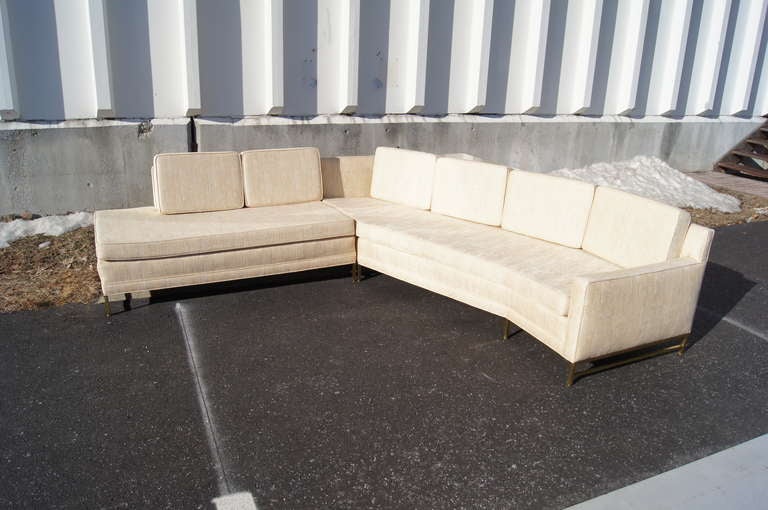 This sectional sofa, designed by Paul McCobb, features three elements: a small armless section; a larger, curved section with one arm; and a travertine-topped table. The table is flush with the back of the sofa, allowing this piece to fit neatly