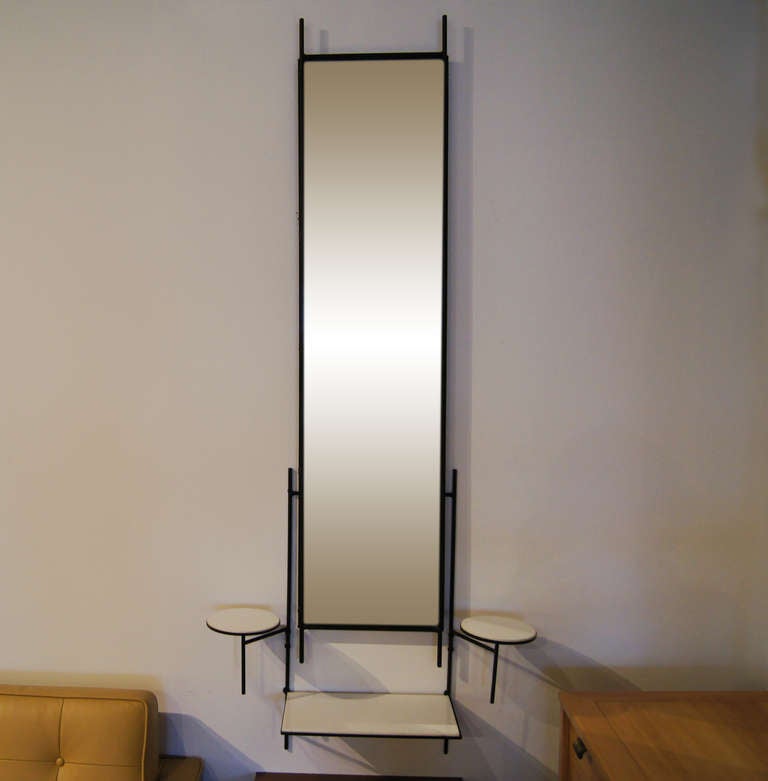 This mirror was designed by Paul McCobb and features two components, a free-hanging mirror and a separate unit, which hangs behind the mirror, with three shelves. The two components are hung separately so they can be positioned at any desired