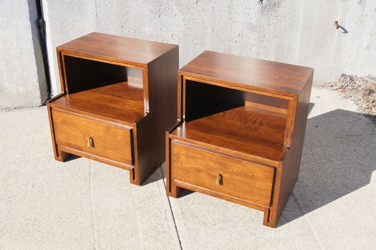 This pair of nightstands was designed by Russel Wright for Conant Ball. Each table features an open shelving area above a deep drawer with a brass pendant drawer pull. The upper shelf measures 22