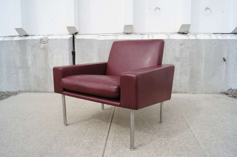 This lounge chair, designed by Hans Wegner, is upholstered in buttery, burgundy leather and features a boxy seat on cylindrical stainless steel legs.