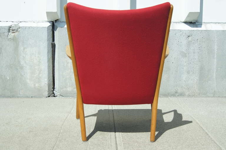 Designed by Hans Wegner in 1951 and produced by A.P. Stolen, this sturdy armchair, model AP16, features an oak frame with a broad curved back and carved armrests. It retains the original red wool upholstery.