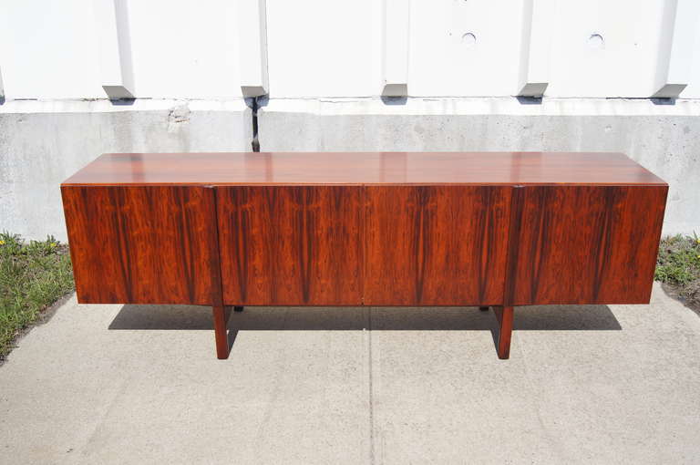 This sideboard, designed by Kofod Larsen, is constructed of beautiful rosewood. Its four drawer, with vertical rosewood drawer pulls, open to reveal two shallow cutlery drawers and seven shelves.