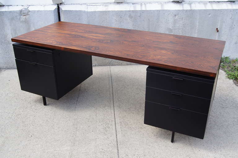 This impressive desk was designed by George Nelson for Herman Miller. It is composed of a stunning rosewood top that is set against black painted drawer units and legs. The left drawer unit features a shallow top drawer with numerous compartments