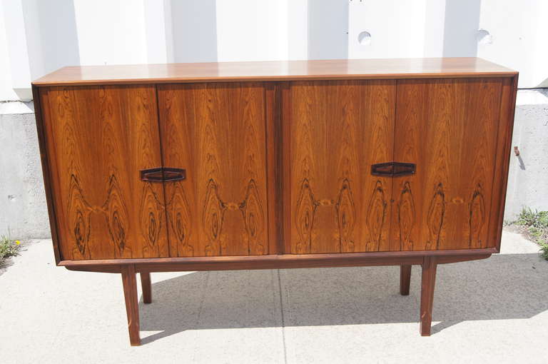 Henry Rosengren Hansen designed this striking rosewood sideboard for NC Møbler. It offers a substantial amount of storage. Its four doors, with graphic inset handles carved from solid rosewood, open to reveal numerous shelves of varying sizes and