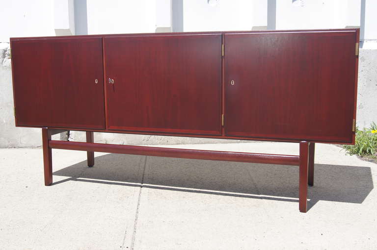 Ole Wanscher designed this modern, clean-lined sideboard as part of his Rungstedlund series for Poul Jeppesen in the 1960s. Constructed of a rich stained mahogany, the raised case features three locking doors (with the original brass key) that