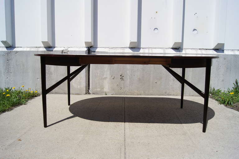 This round dining table, with its beautiful rosewood grain and sculptural base of slender diagonal supports, is exemplary of Mid-Century Danish workmanship. A folding butterfly leaf (47.5 inches wide) transforms the table top into a 79-inch- long
