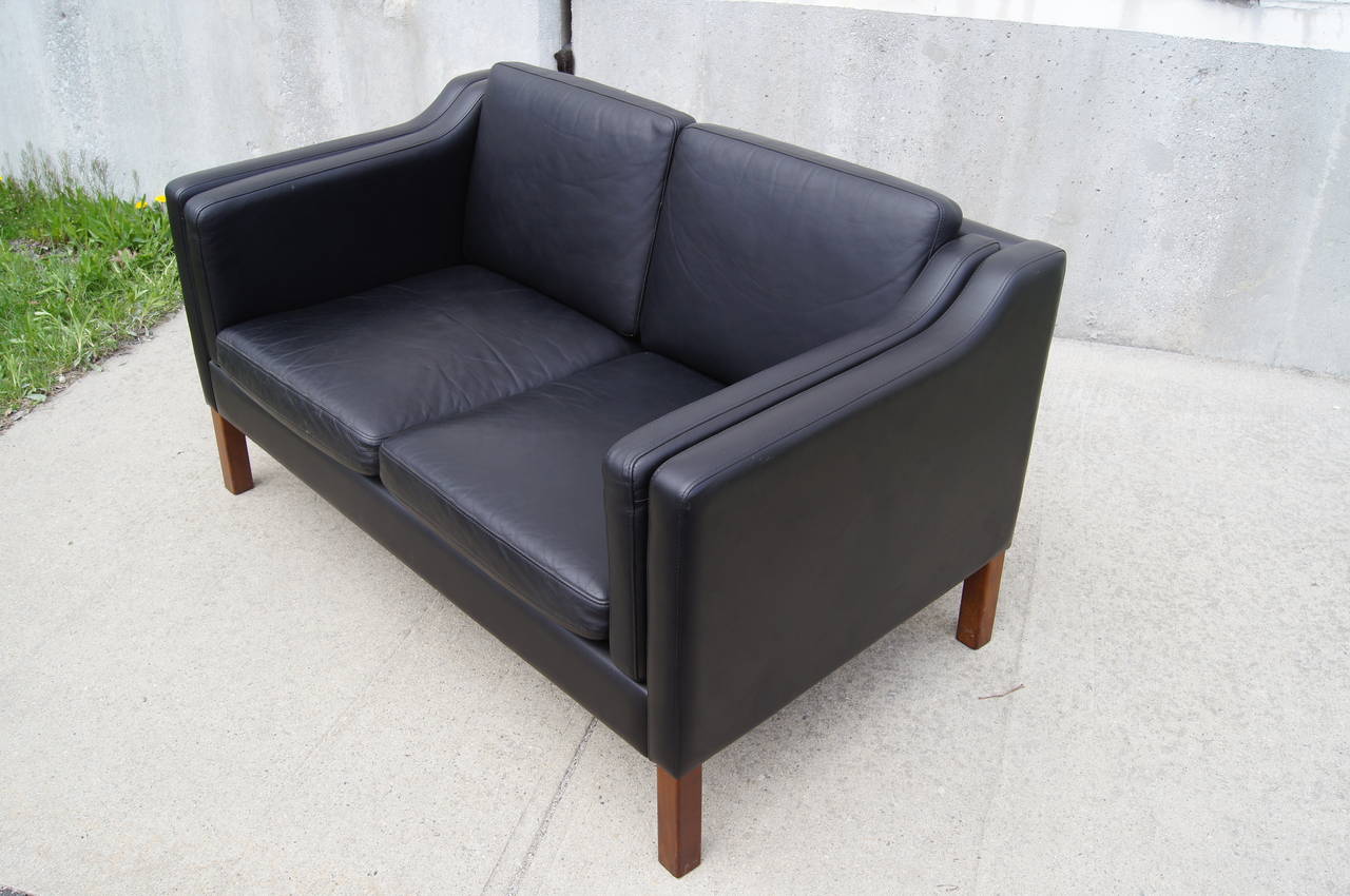 Designed in the manner of Børge Mogensen, this Danish modern settee offers a comfortable seat for two. Upholstered in black leather, it sits on solid wood block legs.