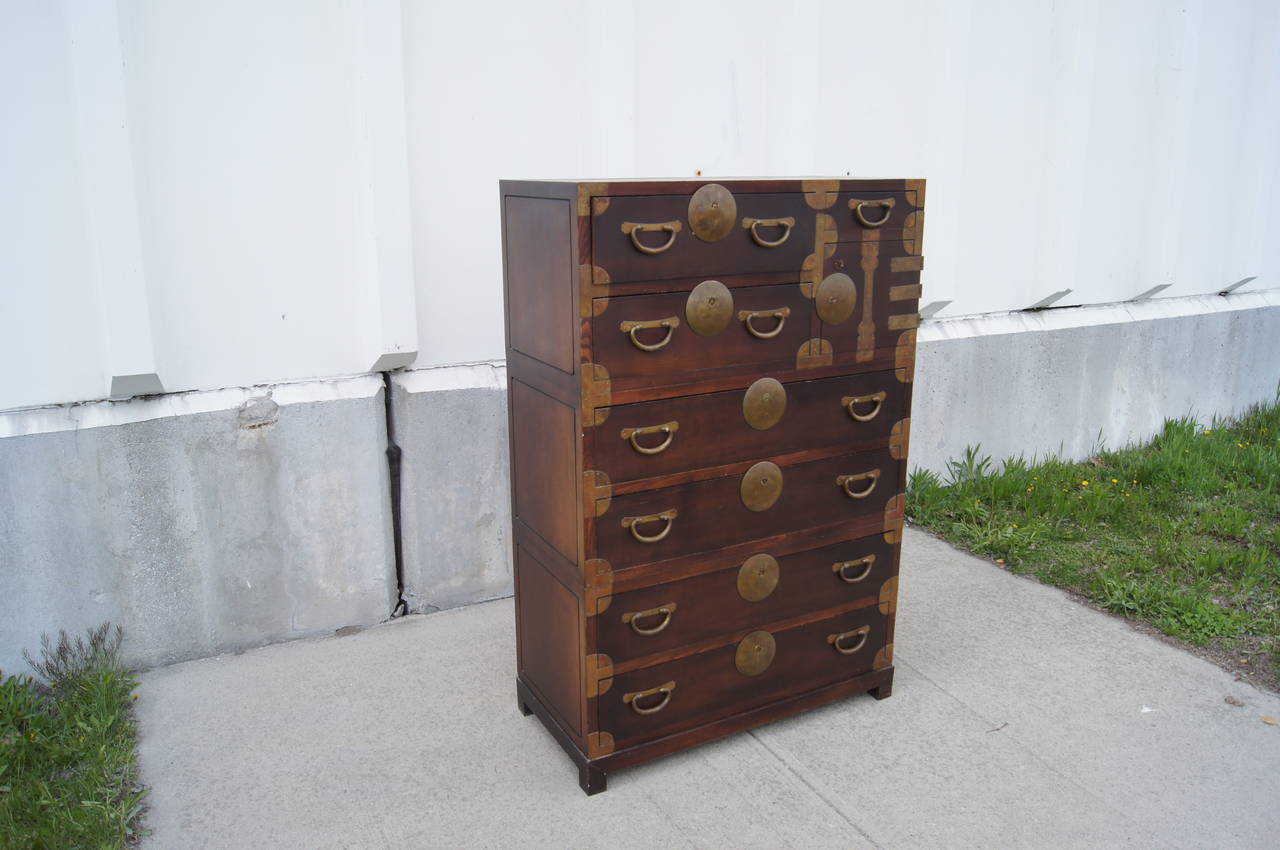 This large, campaign-style chest of drawers was manufactured in the 1950s by John Stuart, a company known for their high-quality pieces that referenced earlier centuries. It comprises four large drawers, two medium drawers, one small drawer, and a