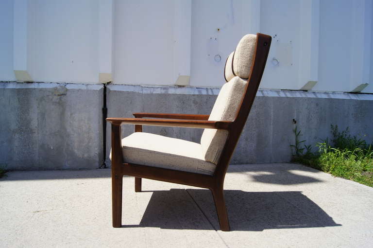 Designed by Hans Wegner and manufactured by GETAMA, this ample lounge chair features a high-back frame of solid oak in a rich, dark stain and features the original off-white upholstery. The headrest attaches to the chair back with leather straps.